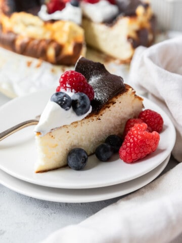 a slice of San Sebastian Cheesecake topped with whipped cream and fruit on a white plate.