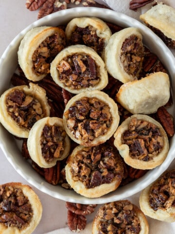 several mini pecan pies in a dish with pecans.