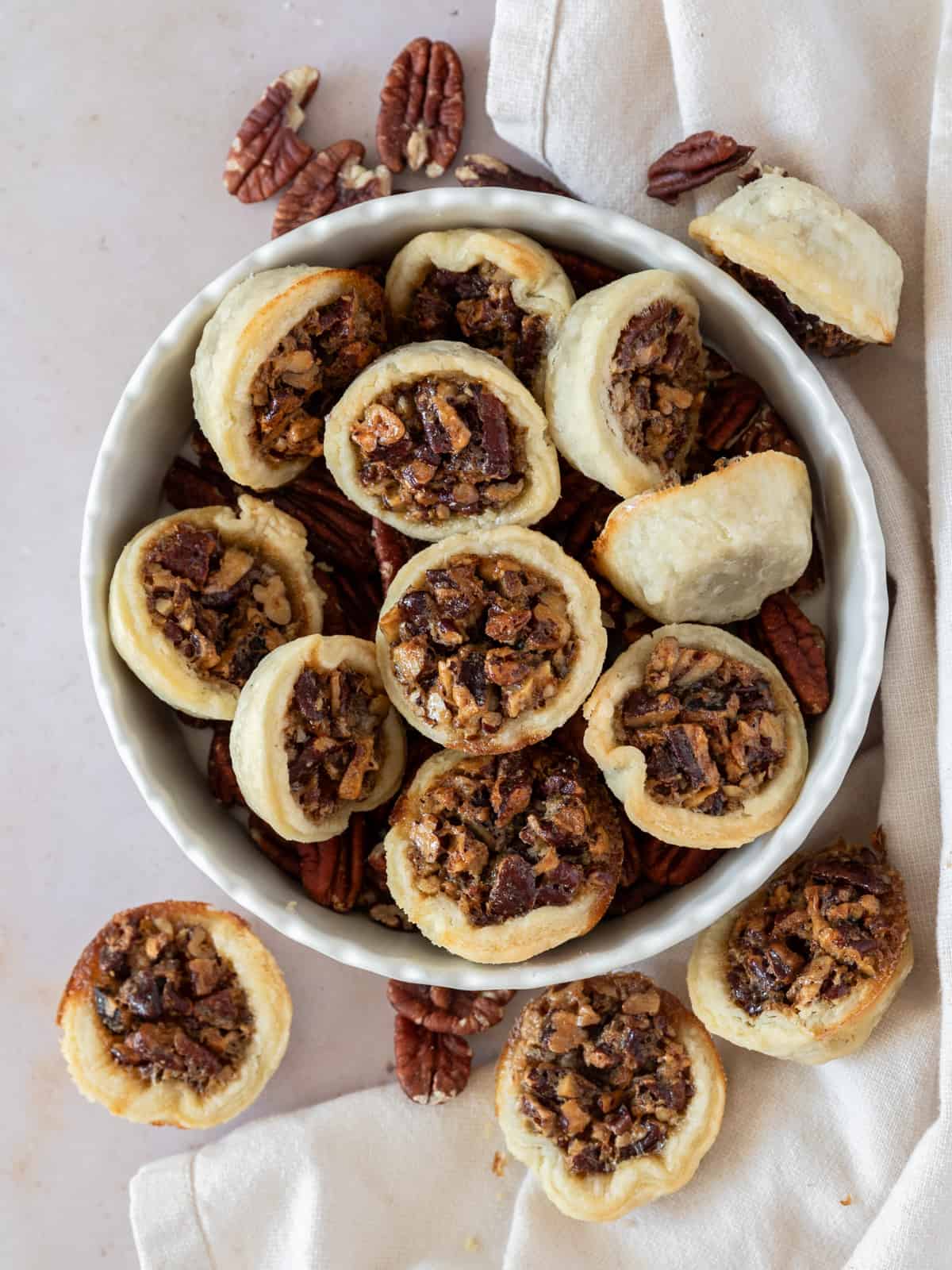 several mini pecan pies in a dish with pecans.