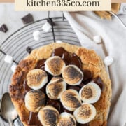 a peanut butter s'mores skillet cookie surrounded by mini marshmallows and chunks of chocolate. It says peanut butter s'mores skillet cookie across the top.