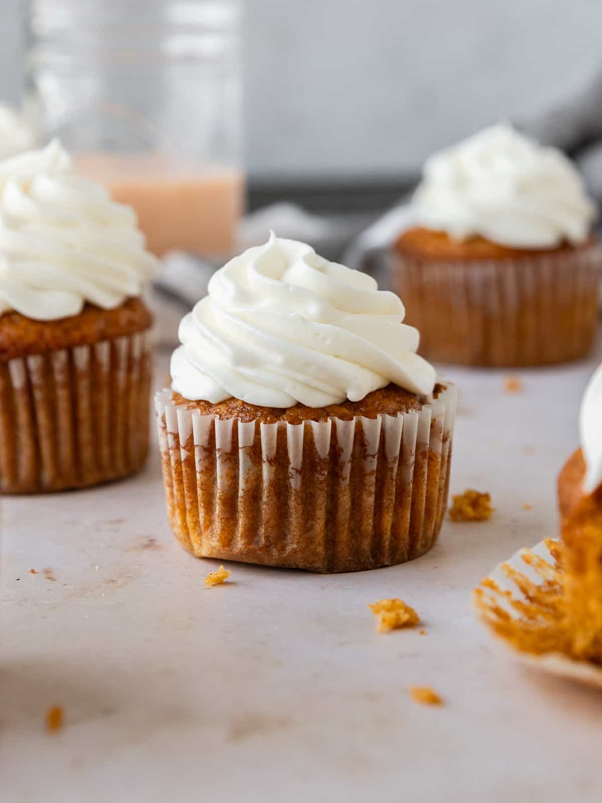 several pumpkin spice cupcakes topped with cream cheese icing on a tan background.