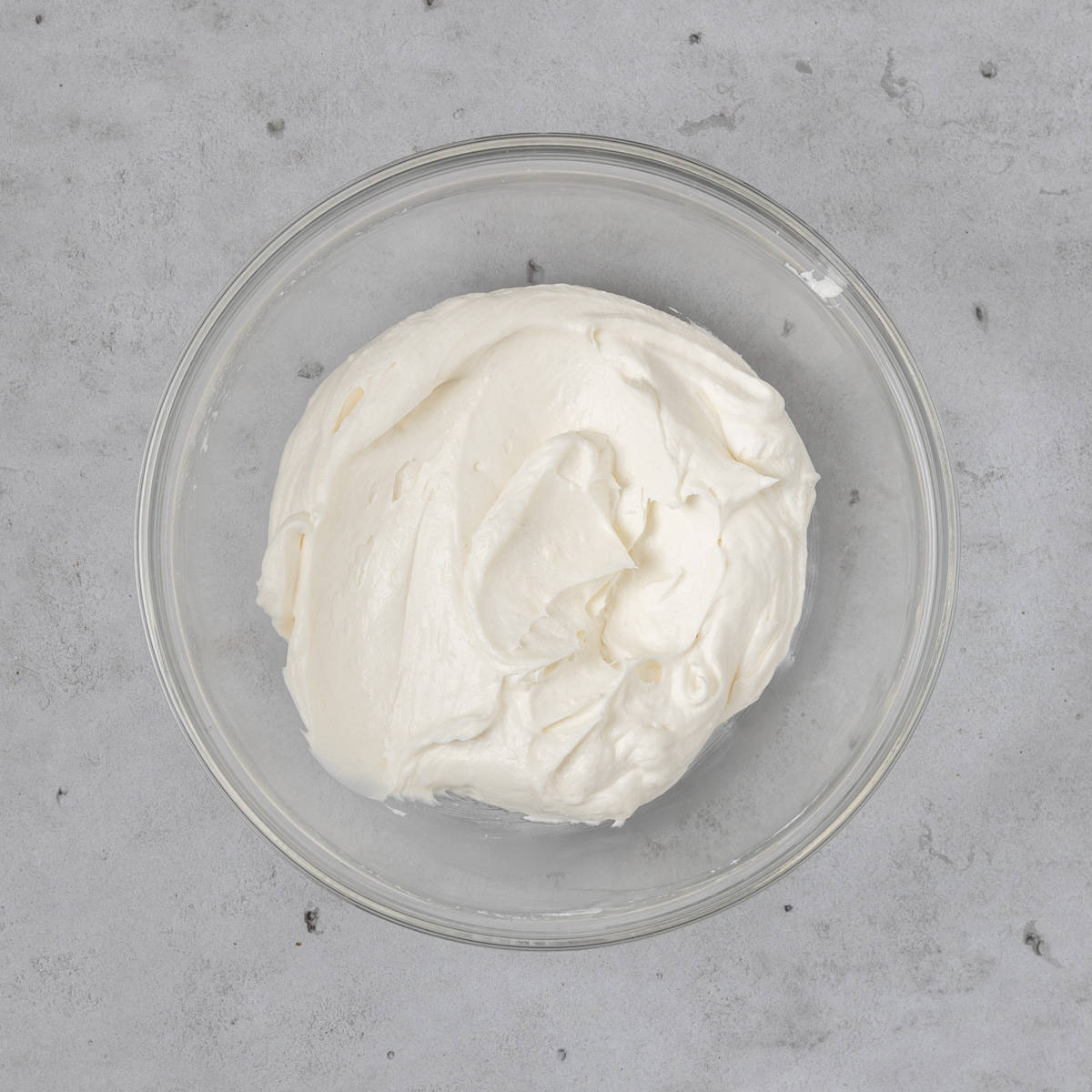 the whipped cream cheese frosting in a glass bowl on a grey background.