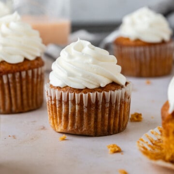 several pumpkin spice cupcakes topped with cream cheese icing on a tan background.