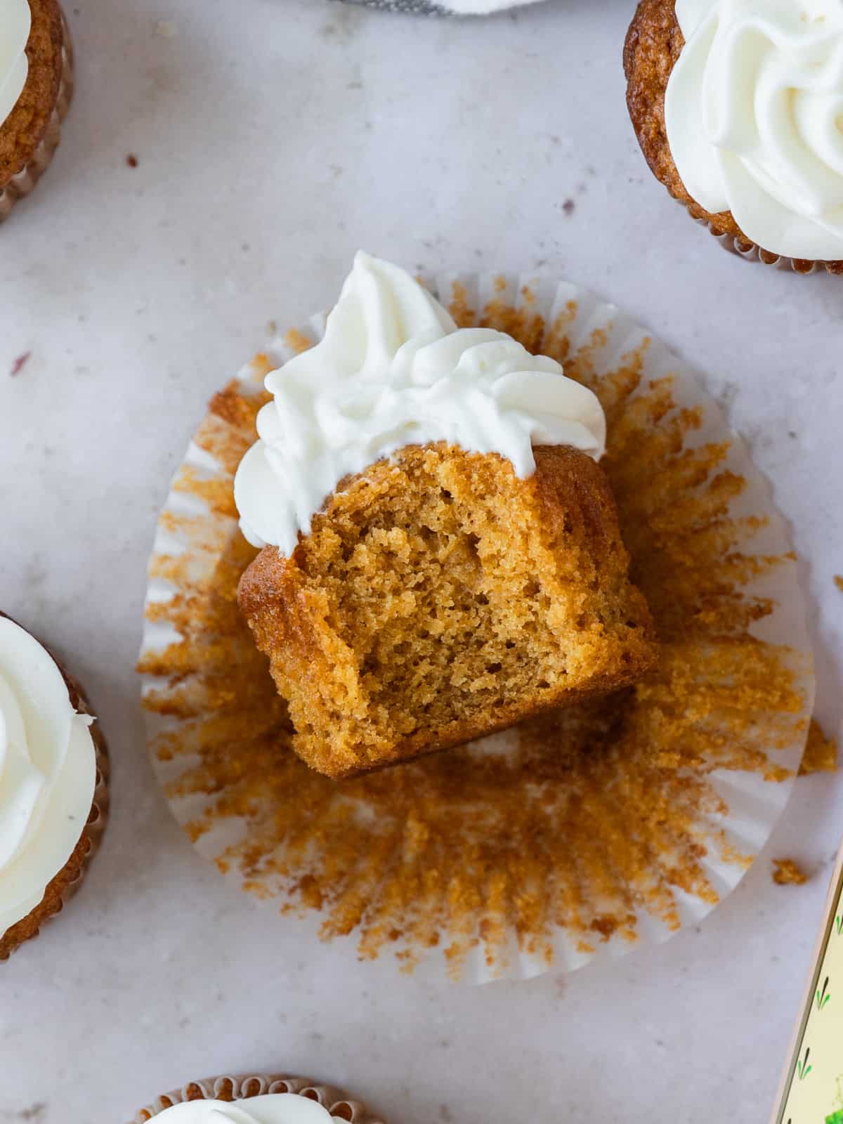 a pumpkin spice cupcake laying on its side with a bite taken out of it.