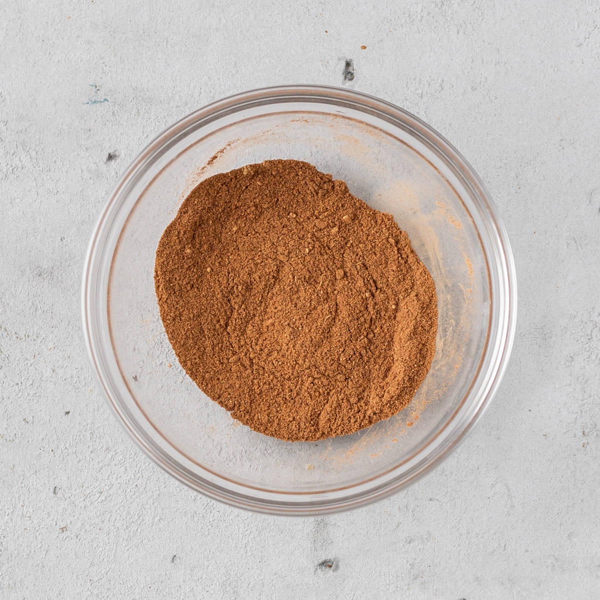 the homemade pumpkin pie spice combined in a glass bowl on a grey background.