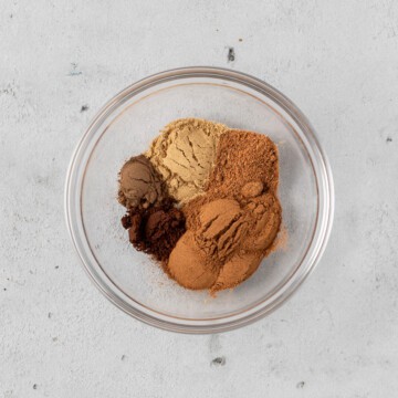 all of the spices scooped into a glass bowl on a grey background.