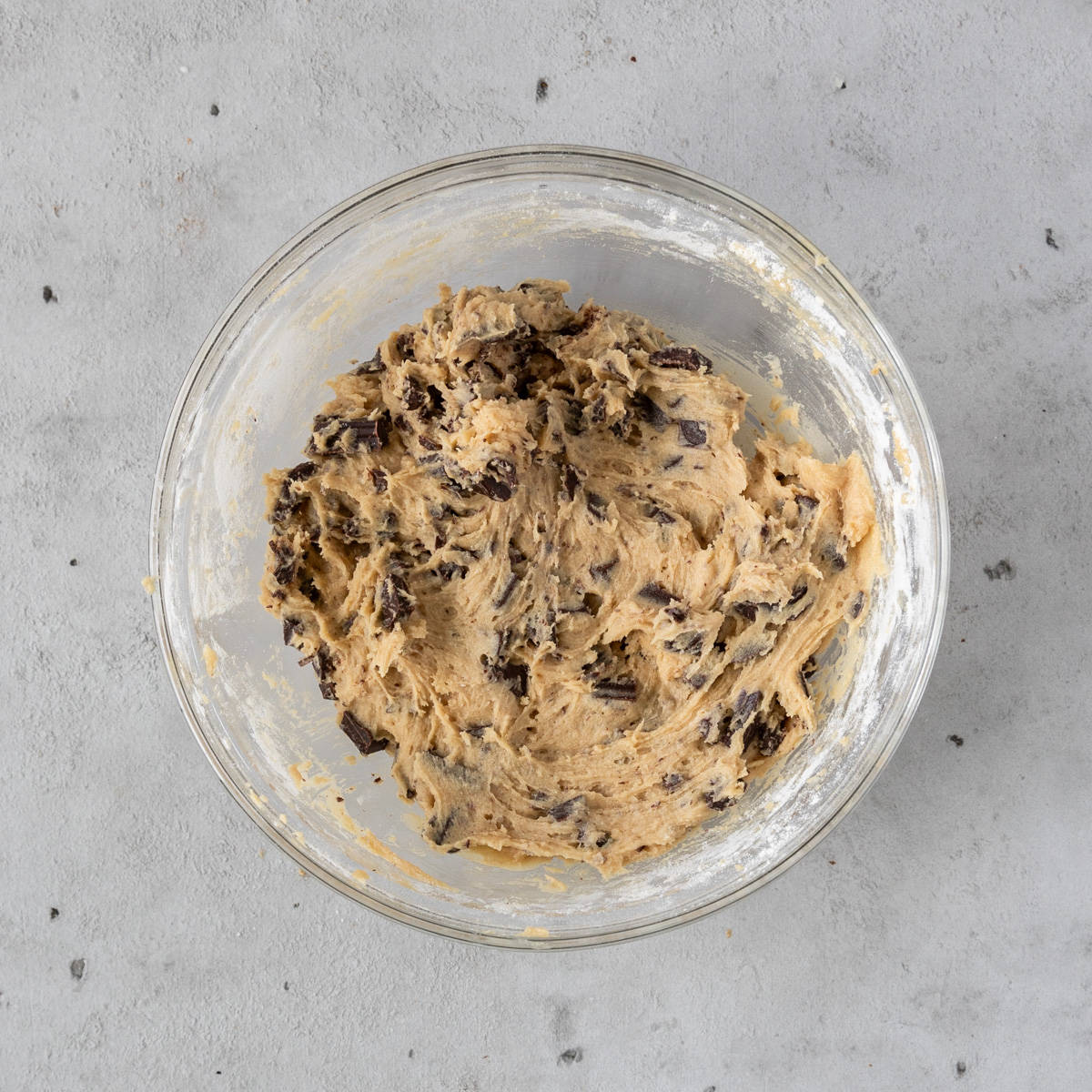 the completed cookie dough in a glass bowl on a grey background.