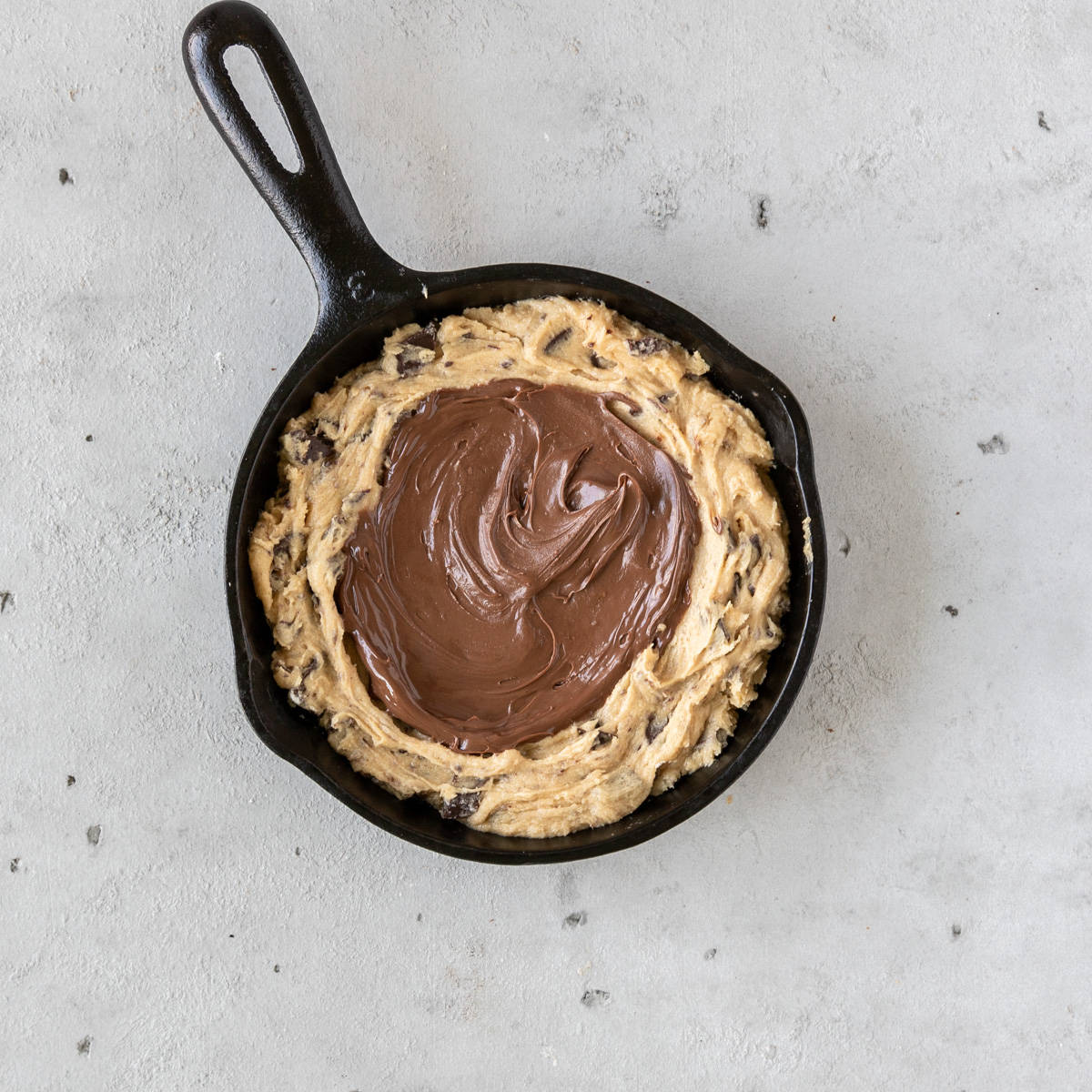 the cookie dough in a cast iron skillet with nutella spread on top of it.