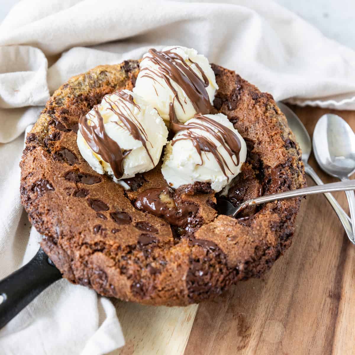 a nutella stuffed skillet cookie topped with ice cream and nutella with a spoon sticking out of it.