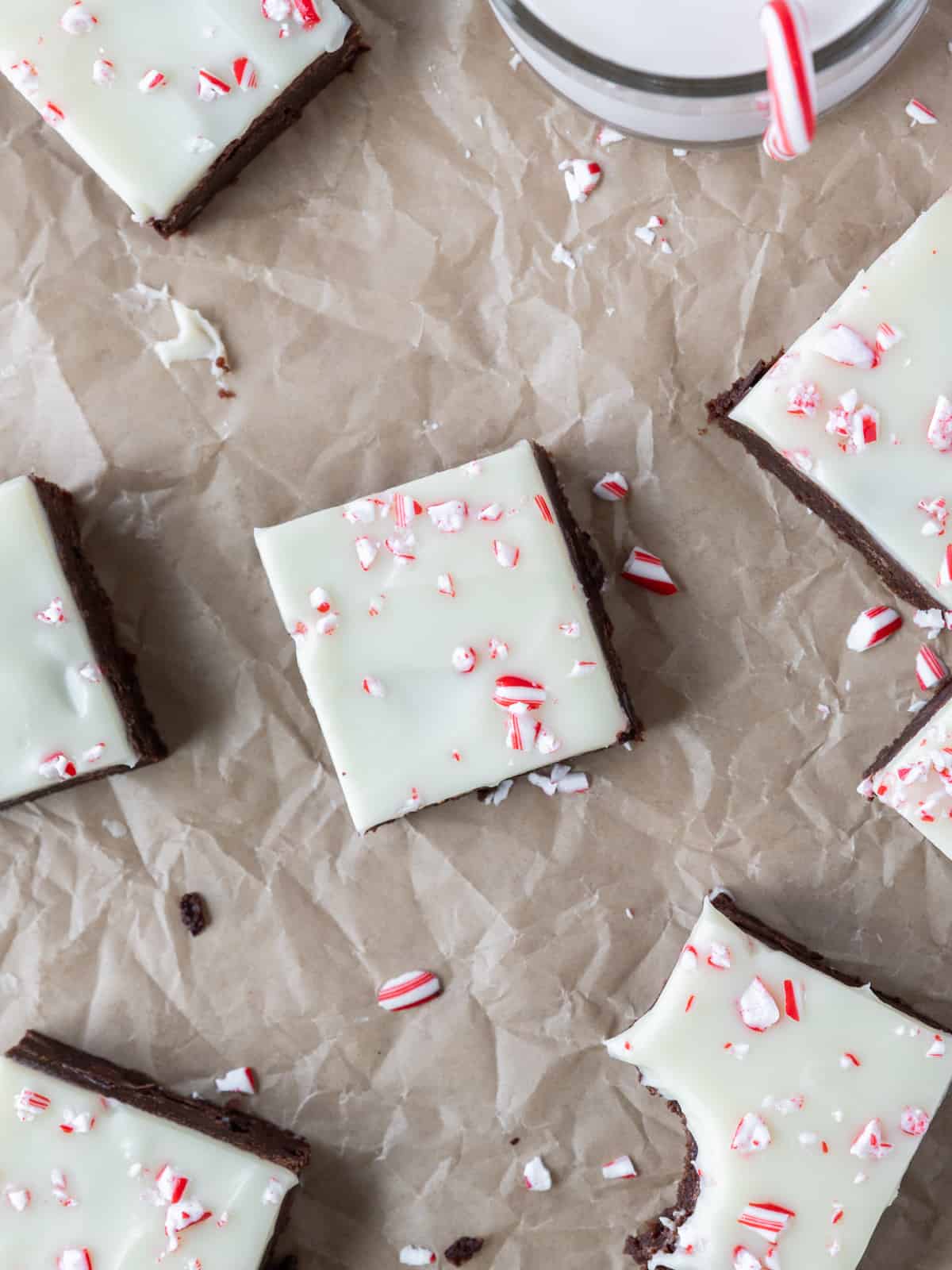 peppermint bark brownies on a brown background with pieces of chocolate and peppermint around it.