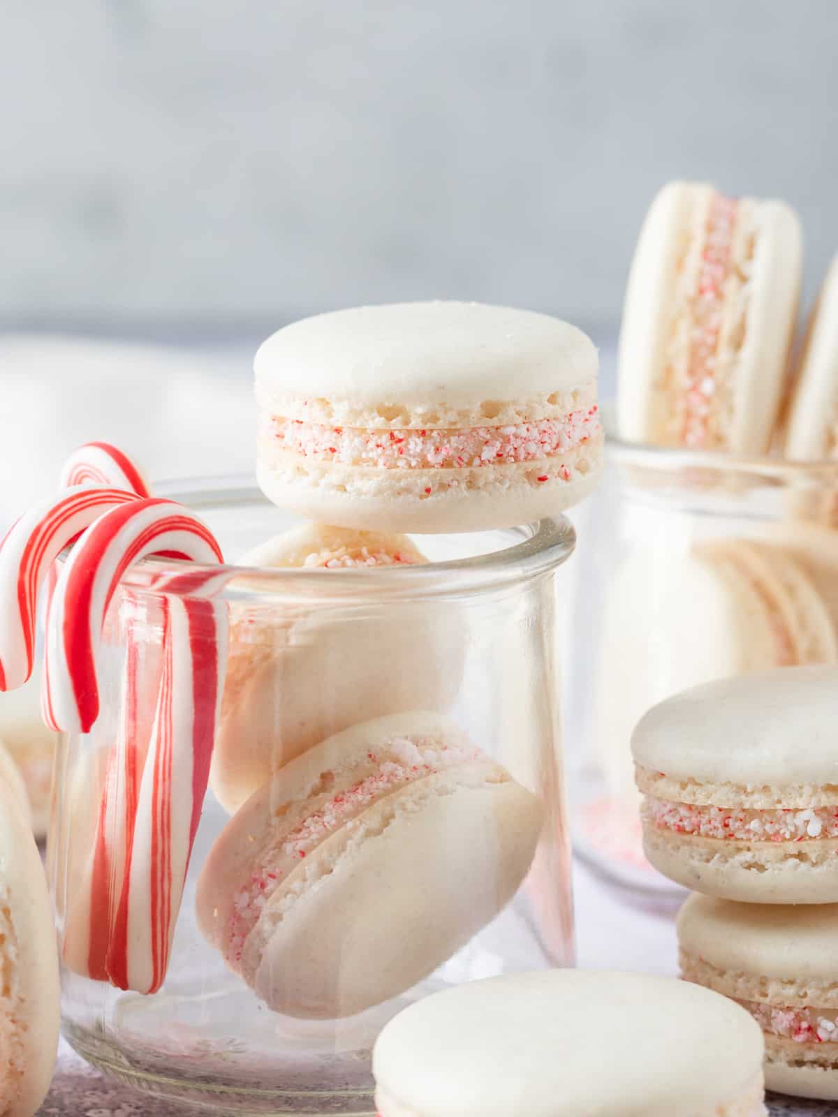 a glass jar filled with peppermint macarons with peppermint candy canes hanging off the side.