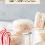a glass jar filled with peppermint macarons with peppermint candy canes hanging off the side. It says peppermint macarons across the top.