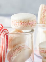 a glass jar filled with peppermint macarons with peppermint candy canes hanging off the side.