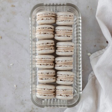 two lines of pumpkin spice macarons in a glass dish on a tan background.