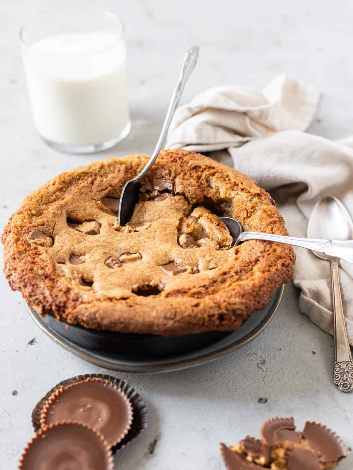 a reese's cookie skillet with two spoon stuck in it and peanut butter cups around it.
