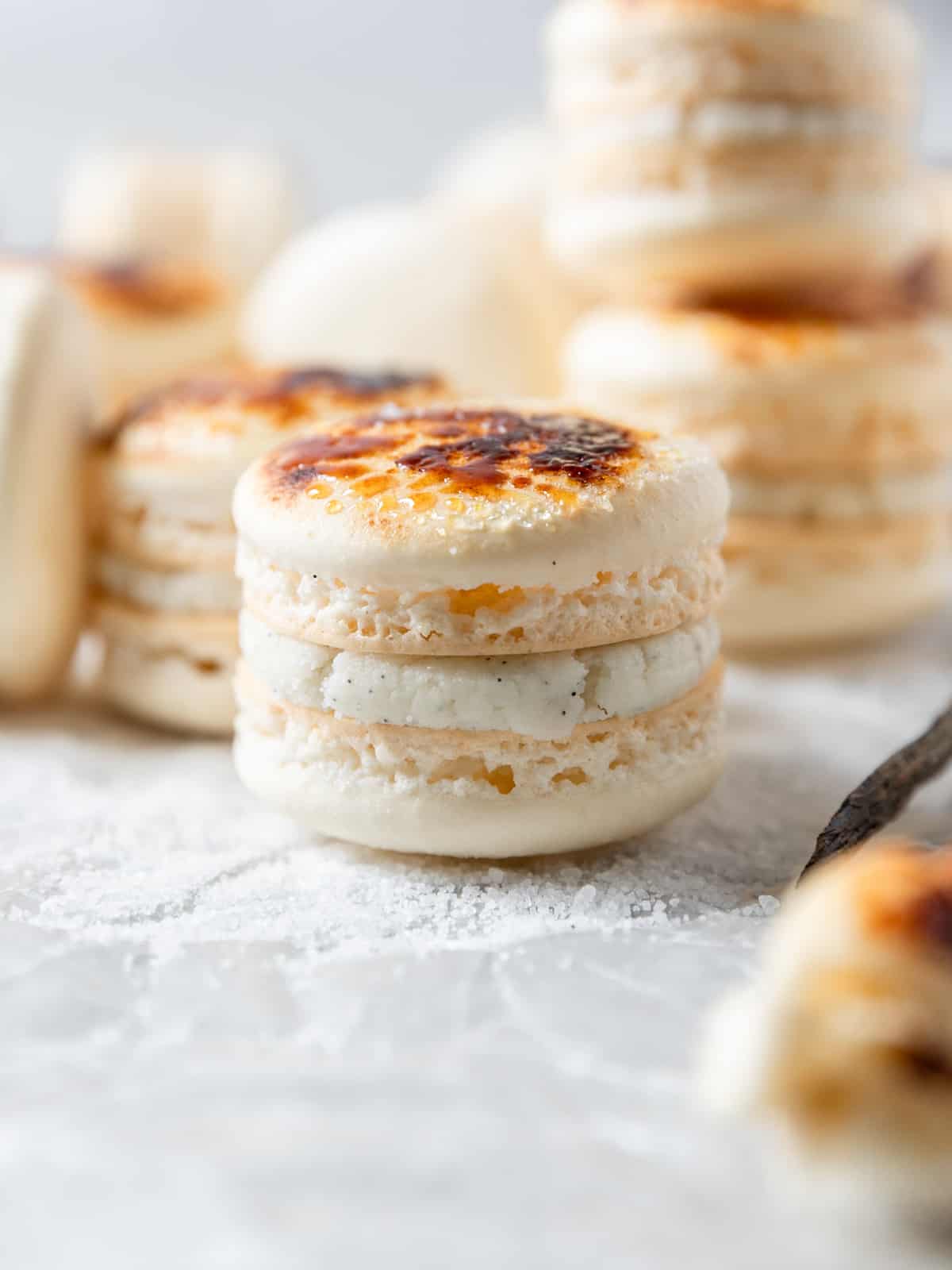 a creme brûlée macaron on a bed of sugar with several other macarons behind it.