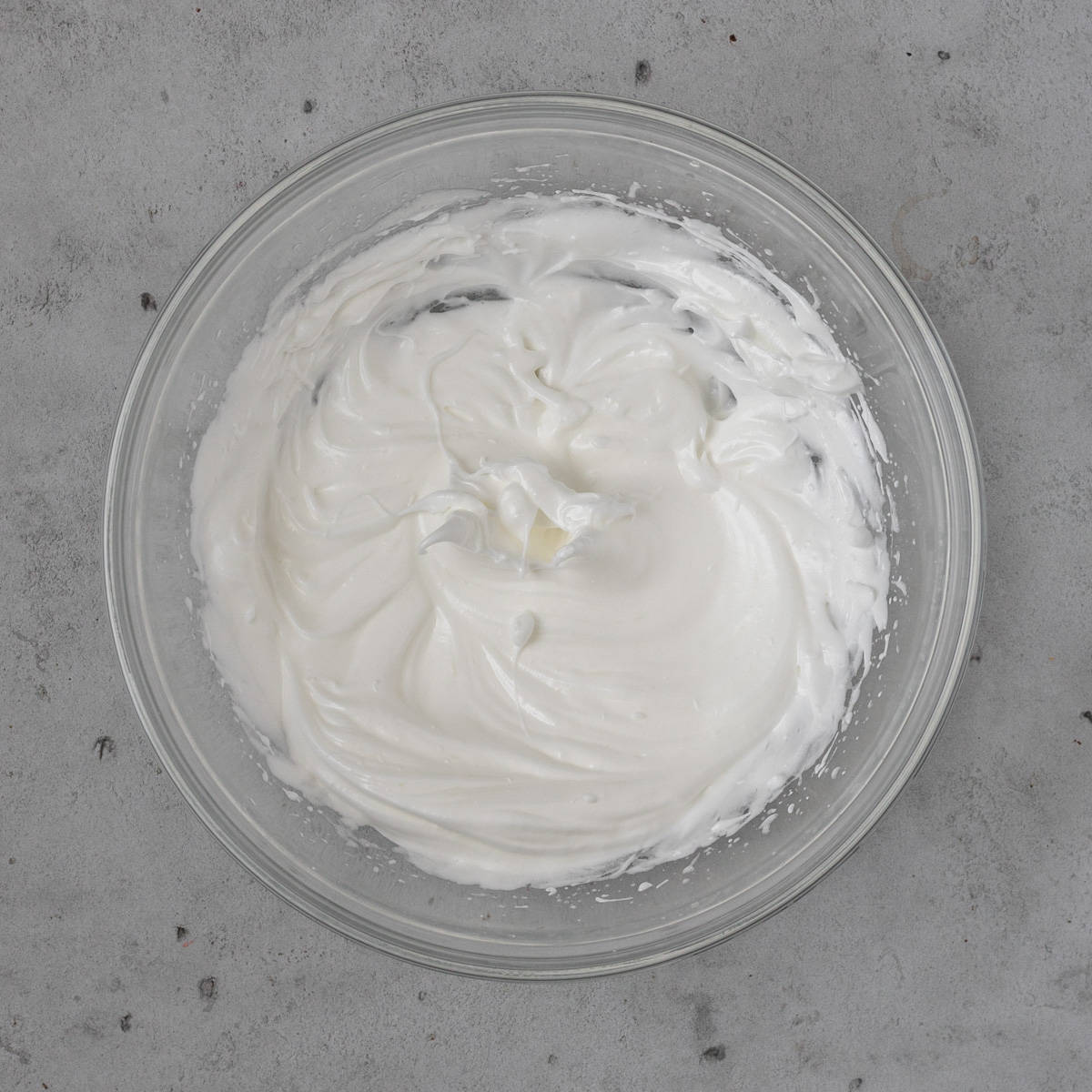 the french meringue in a glass bowl on a grey background.