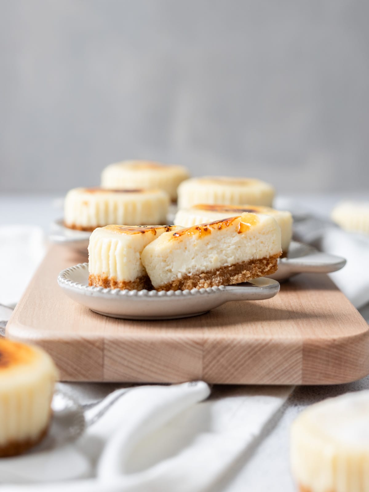 several mini creme brûlée cheesecakes on a wooden serving board. One is cut in half.