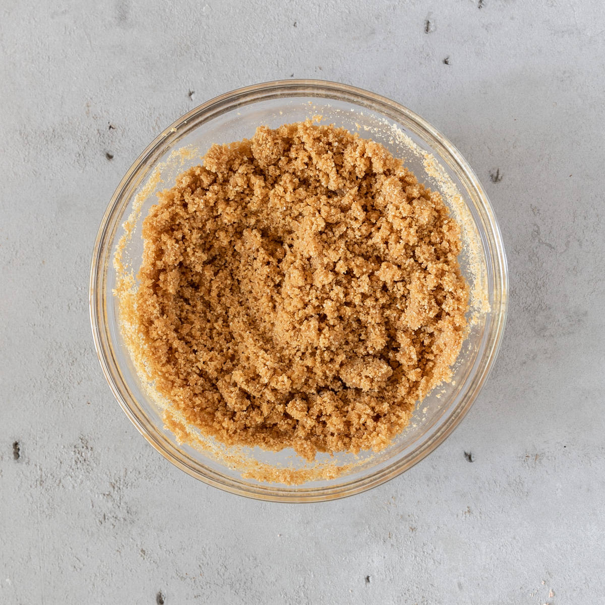 the graham cracker crust ingredients combined in a glass bowl on a grey background.