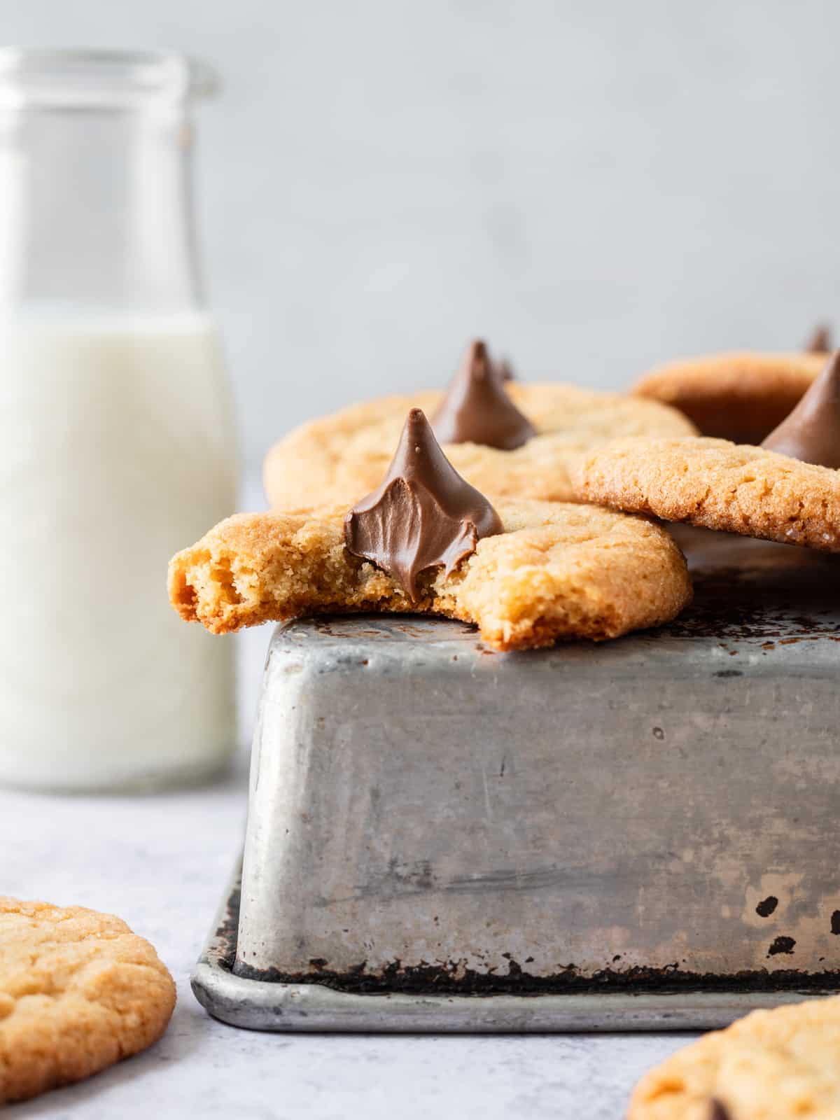 a peanut butter blossom with a bite out of it balancing on a metal baking dish.