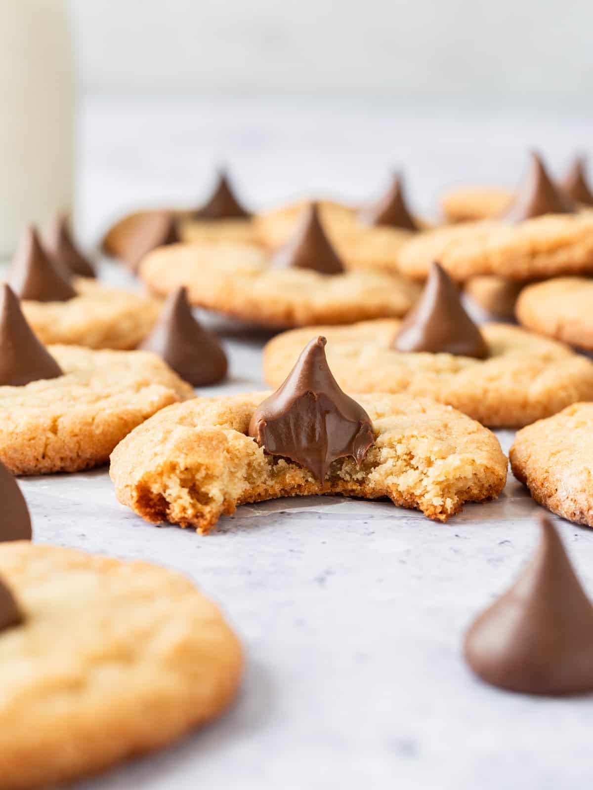 peanut butter blossoms spread out on a grey background, one has a bite out of it.