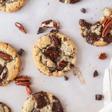 several pecan chocolate chip cookies surrounded by pecans and chunks of chocolate.