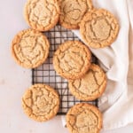 several almond flour peanut butter cookies spread out on a small wire rack with a linen napkin under it.