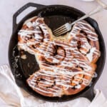 apple pie filled cinnamon rolls in a cast iron pan with a two taken out of the pan.