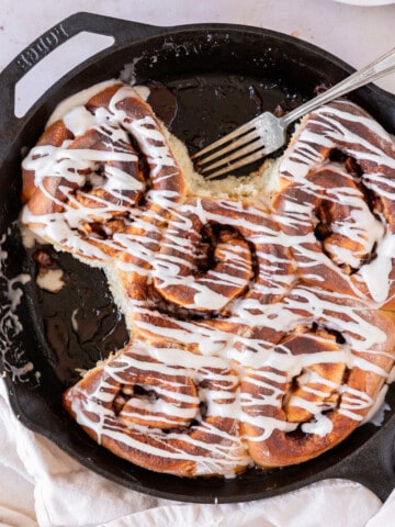 apple pie filled cinnamon rolls in a cast iron pan with a two taken out of the pan.
