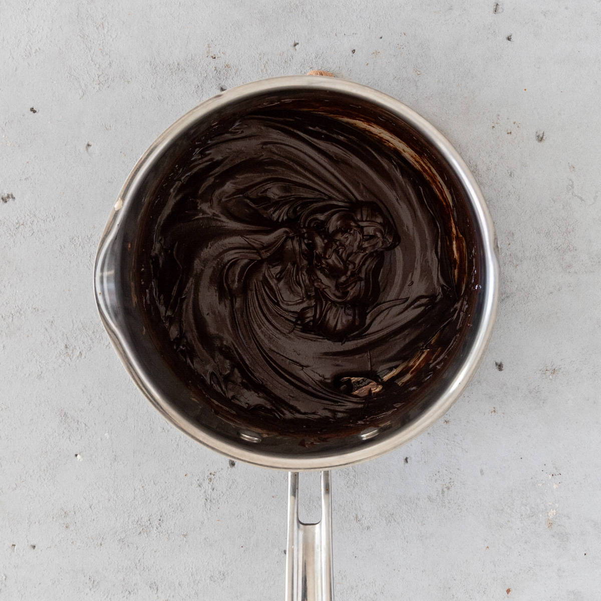 the chocolate ganache in a small pot on a grey background.