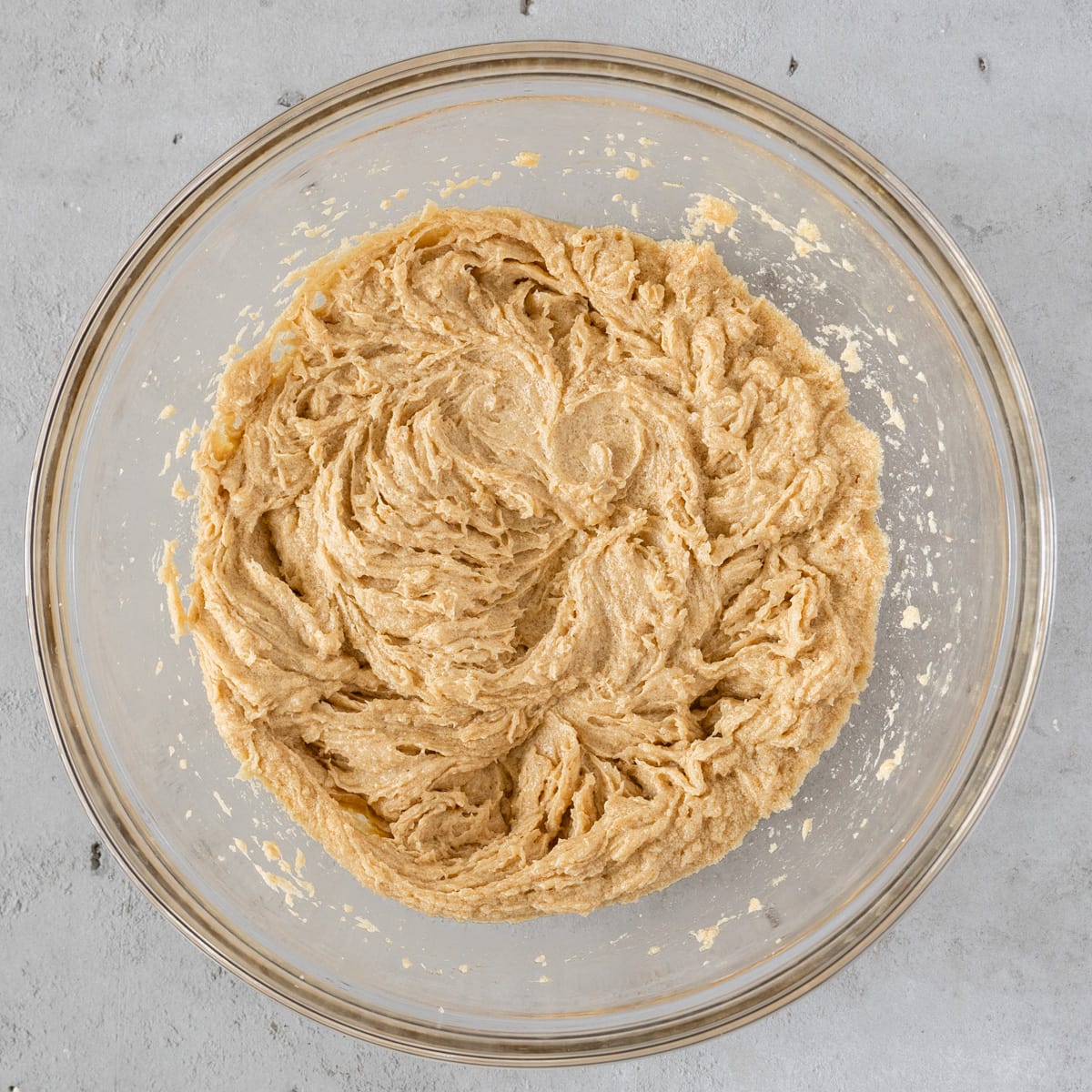 the wet ingredients and sugars combined in a glass bowl on a grey background.