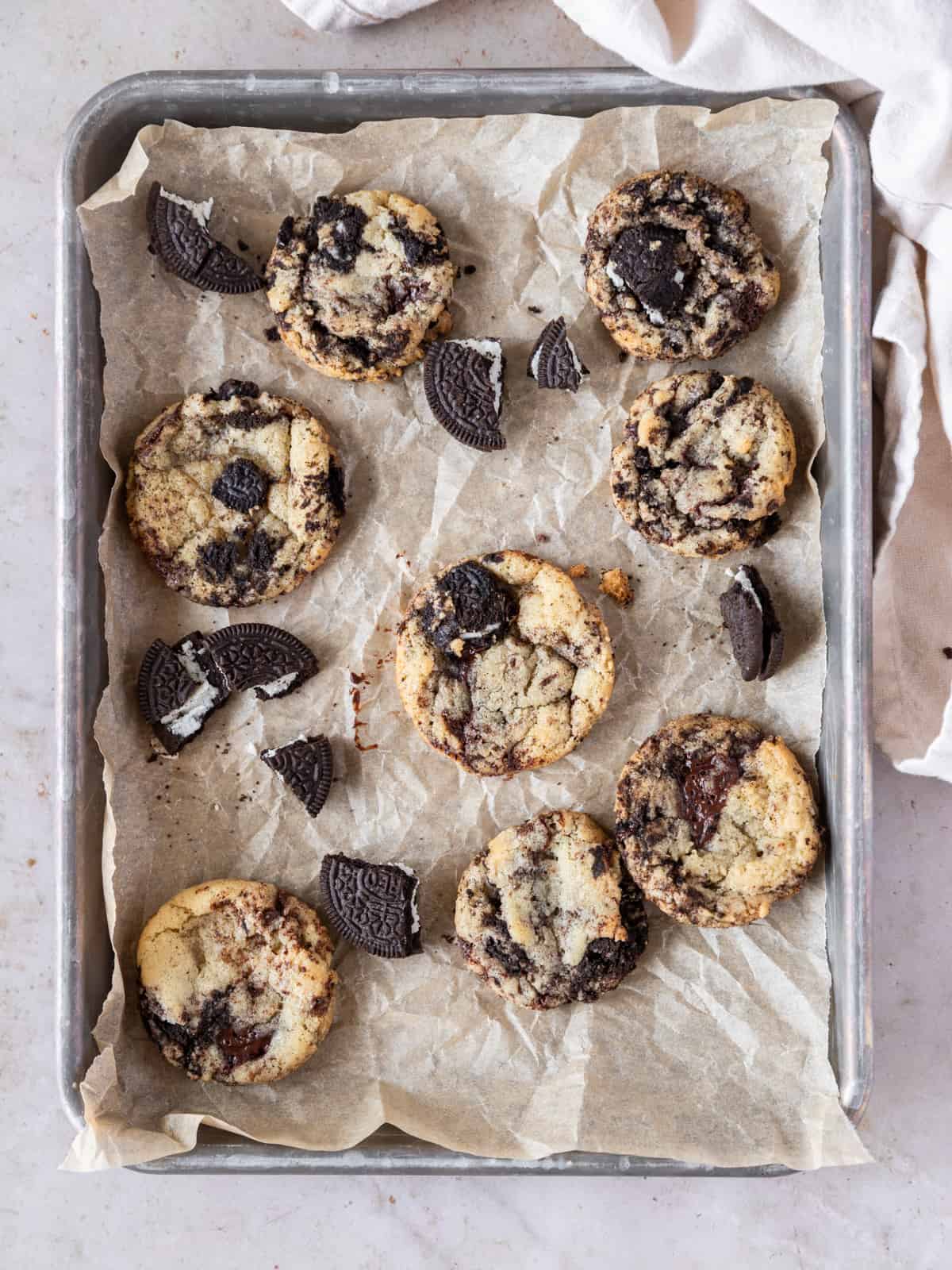 several oreo and chocolate chip cookies and oreos on a metal sheet pan with parchment paper.