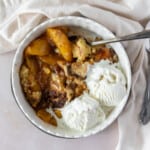 peach cobbler with cake mix in a white dish topped with two scoops of vanilla ice cream.