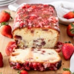 a strawberry pound cake on a cutting board with one slice laying in front of it and strawberries all around.