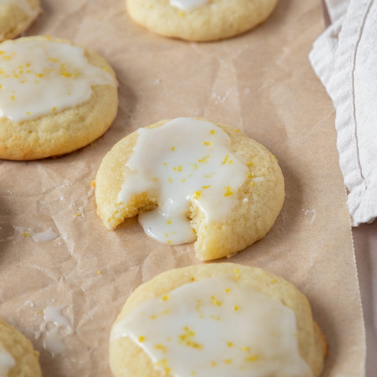 several lemony ricotta cookies topped with lemon glaze on parchment paper, one has a bite out of it.