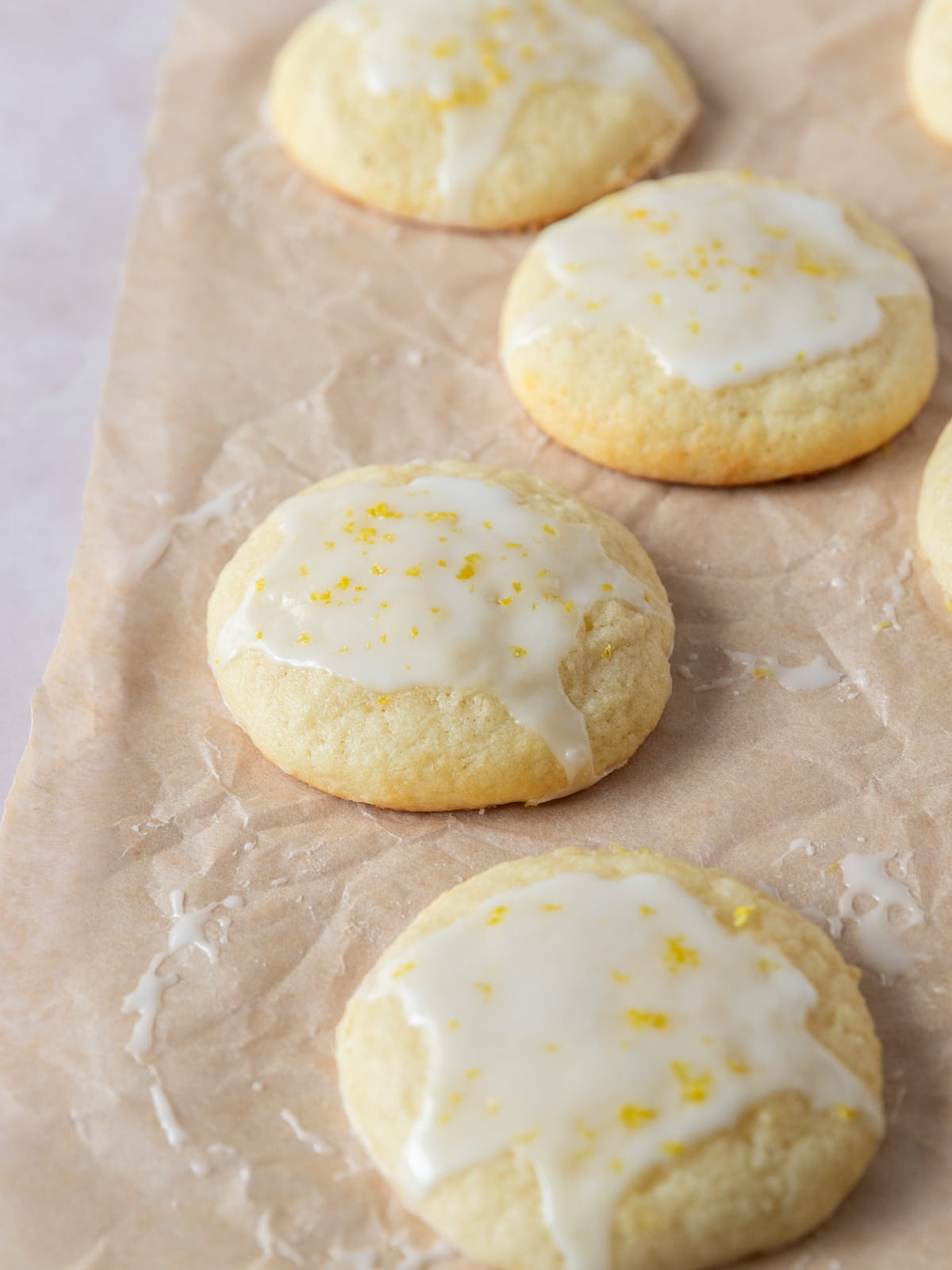 Lemony ricotta cookies topped with lemon glaze on parchment paper.