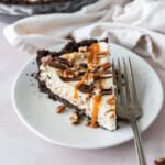 A slice of turtle pie on a white plate drizzled with caramel and chocolate sauce.