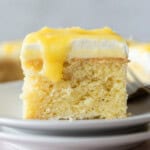 a slice of lemon curd cake on top of two stacked white plates with a drip of lemon curd coming down the side.