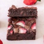a strawberry brownie with another brownie leaning on top of it and fresh strawberries around it.