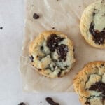 a chocolate chip cookie without brown sugar on a piece of parchment paper surrounded by other cookies and chunks of chocolate.