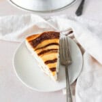 a slice of Cinnamon Roll Cheesecake on a white plate with a fork next to it.