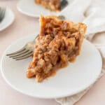 a slice of french apple pie on a white plate with a fork next to it.