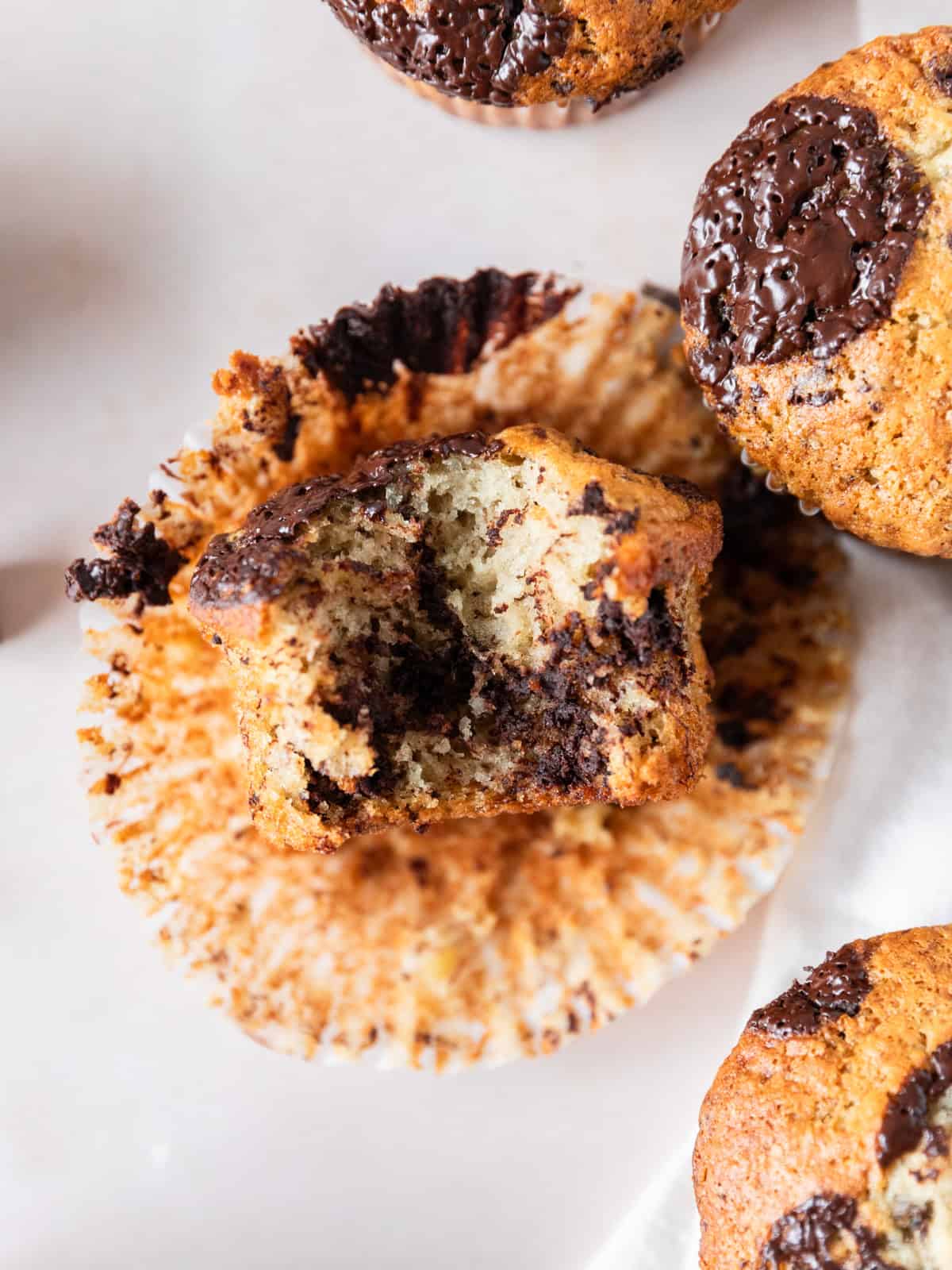 a banana chocolate chunk muffins laying on its side with a bite out of it on a muffin liner with other muffins around it.