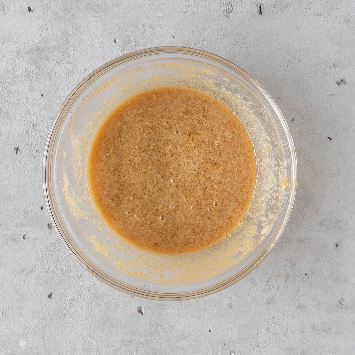 the wet ingredients and sugar combined in a glass bowl on a grey background.