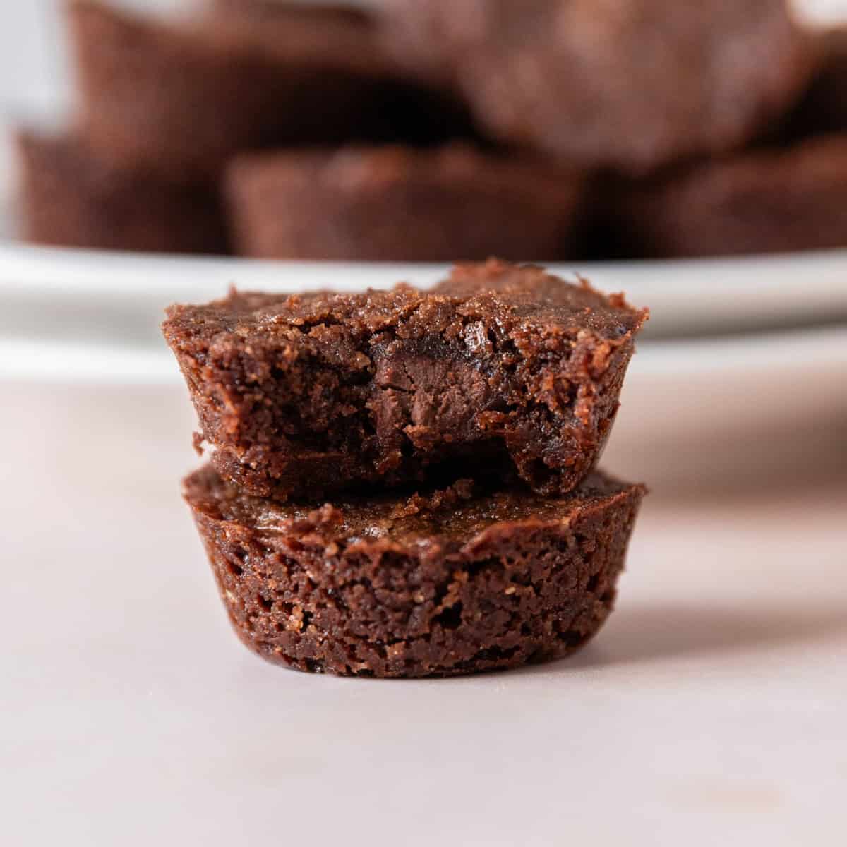 two brownie bites stacked on top of one another. One has a bite out of it.