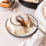 a cinnamon roll on a white plate with a bite taken out of it.