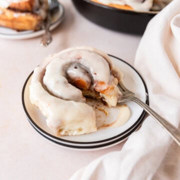 a cinnamon roll on a white plate with a bite taken out of it.