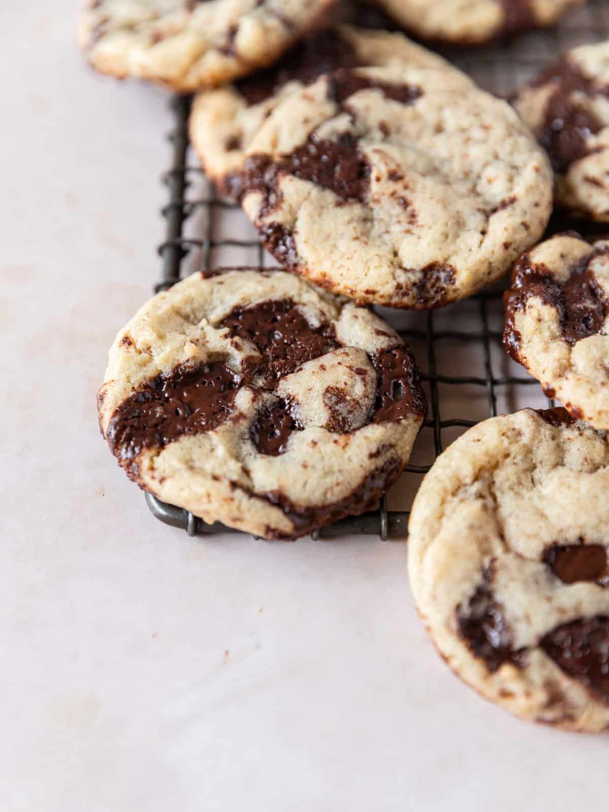 several sourdough chocolate chip cookies on the edge of a metal cooling rack.