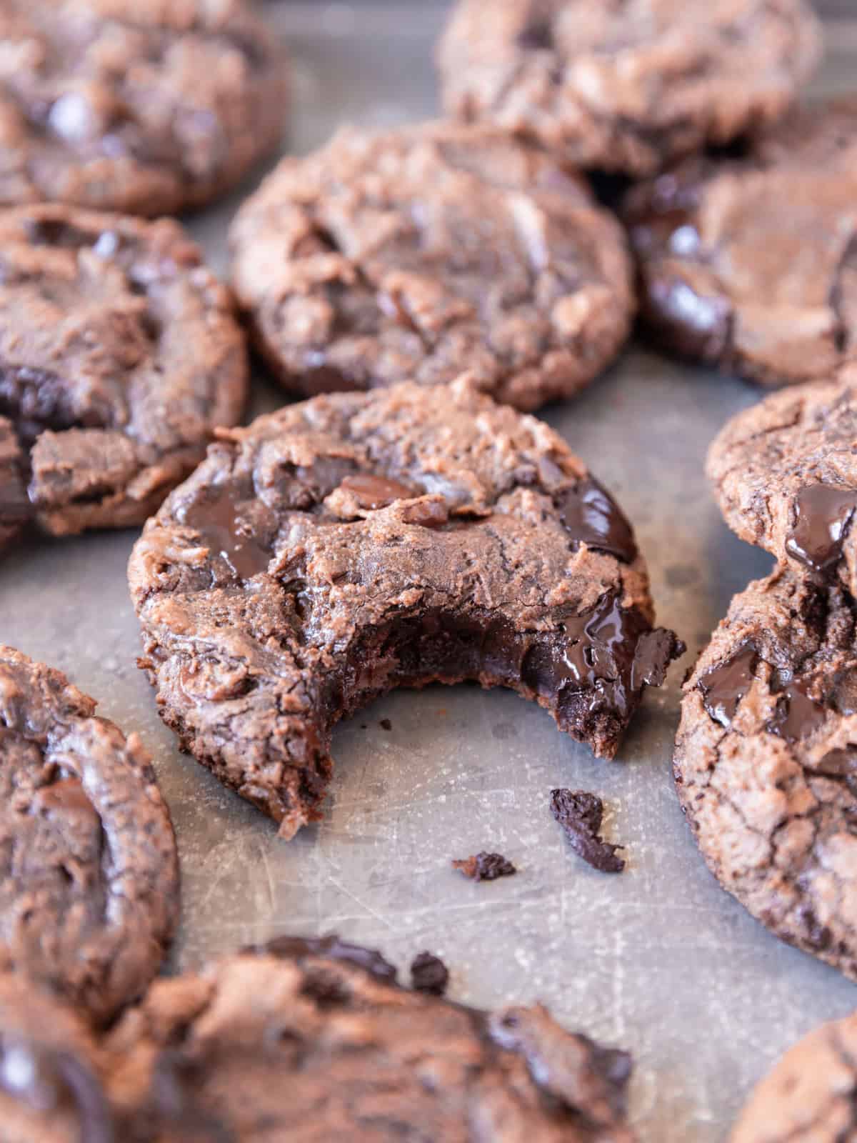 a metal baking dish full of brownie mix cookies and one has a bite out of it.