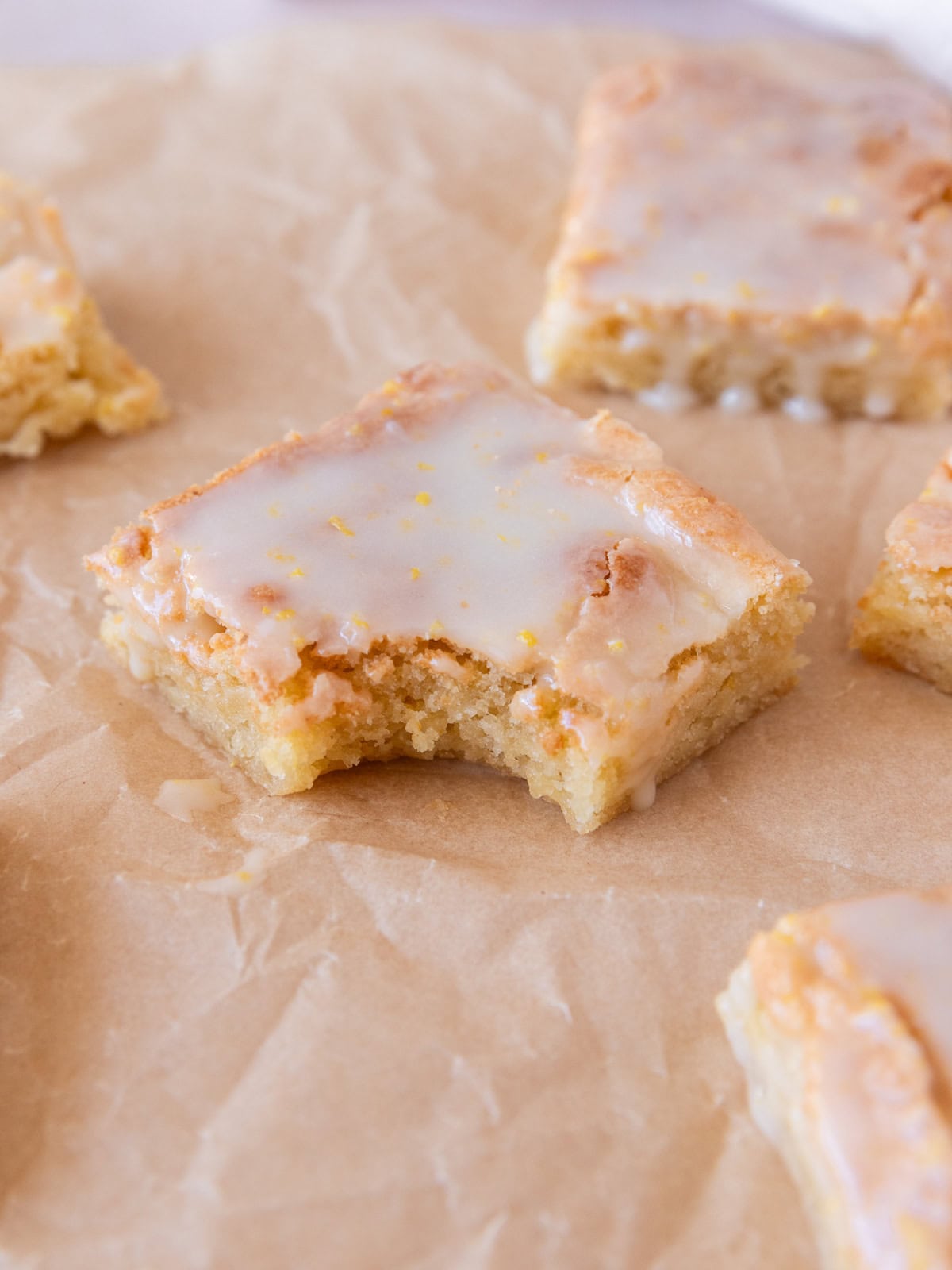 several lemon brownies on a piece of parchment paper. One has a bite out of it.